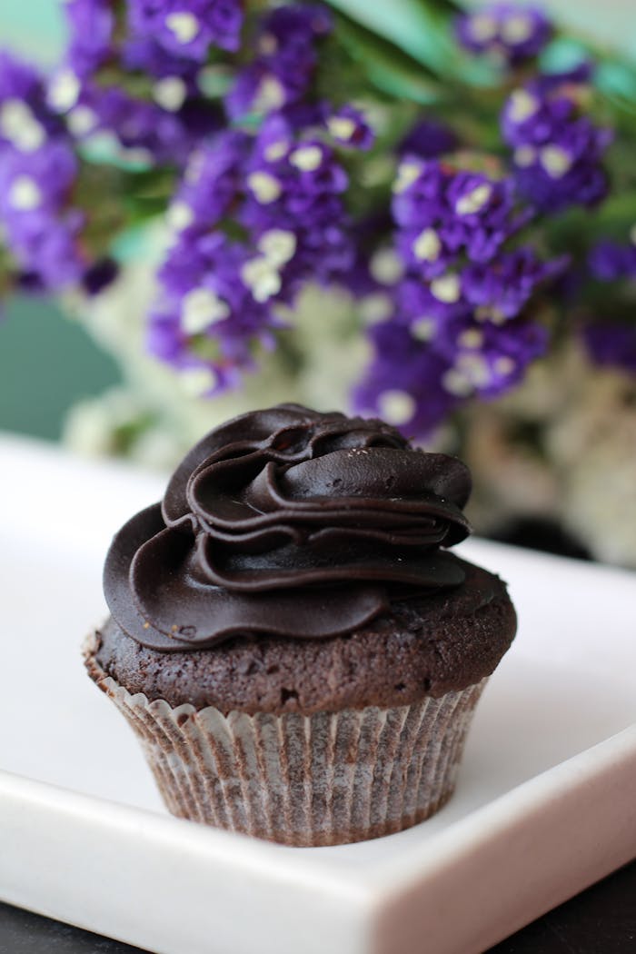 A rich chocolate cupcake topped with creamy icing and a floral backdrop.